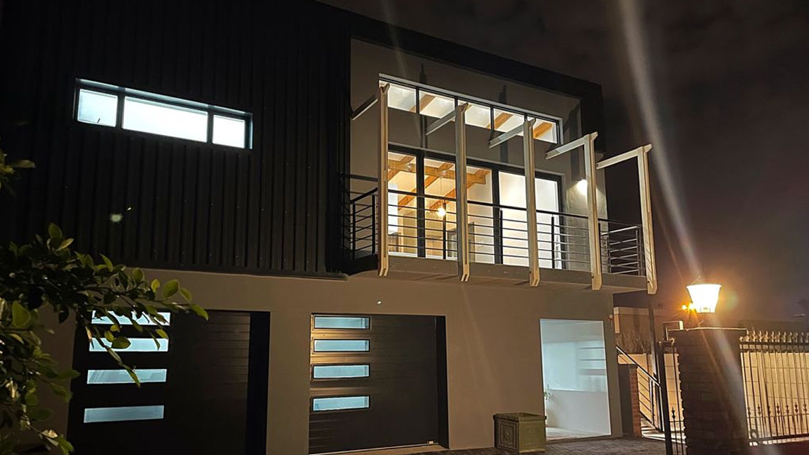 Completed modern double-story home by Prism Construction in Framesby, Port Elizabeth, featuring an entrance staircase with rails, architectural timber siding, and aluminium stacker doors with integrated security gates.